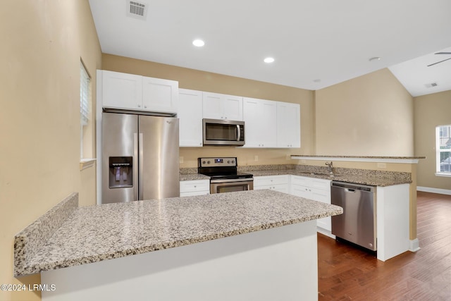 kitchen featuring appliances with stainless steel finishes, white cabinetry, light stone countertops, dark hardwood / wood-style flooring, and kitchen peninsula