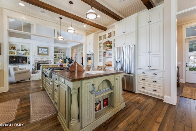 kitchen with appliances with stainless steel finishes, wood counters, white cabinetry, a kitchen island with sink, and beam ceiling