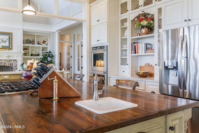 kitchen featuring sink, appliances with stainless steel finishes, built in features, a fireplace, and white cabinets