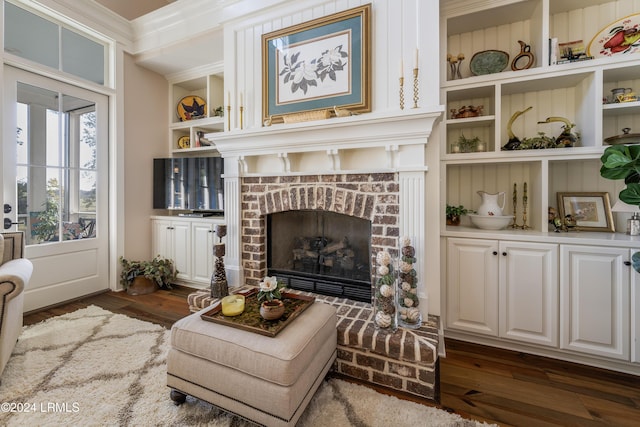 living area featuring crown molding, a fireplace, built in features, and dark hardwood / wood-style floors