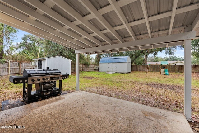 view of patio featuring a playground, a fenced backyard, an outdoor structure, a grill, and a storage unit