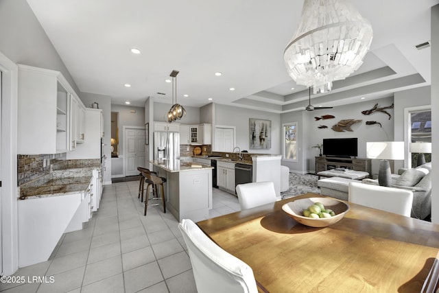 tiled dining area with ceiling fan with notable chandelier and a raised ceiling