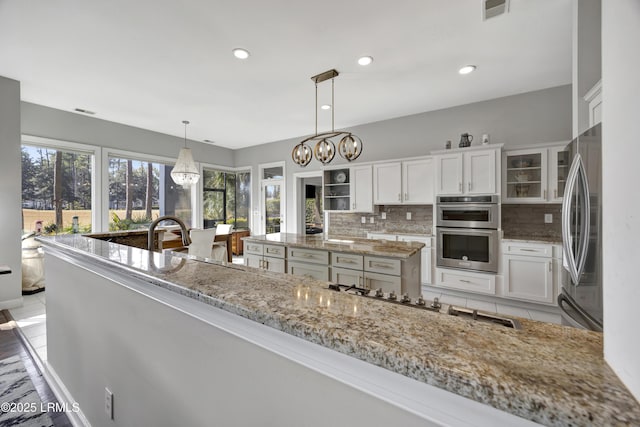 kitchen with light stone counters, stainless steel appliances, decorative light fixtures, and white cabinets