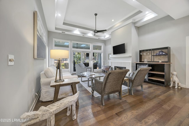 living room featuring a tile fireplace, ornamental molding, ceiling fan, a raised ceiling, and dark wood-type flooring