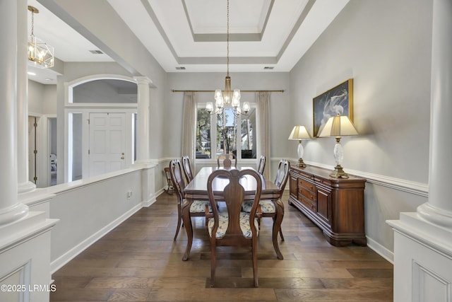 dining space featuring an inviting chandelier, a tray ceiling, dark wood-type flooring, and decorative columns