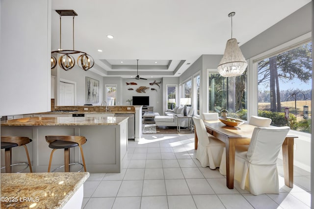 kitchen featuring a wealth of natural light, sink, hanging light fixtures, light stone counters, and a tray ceiling