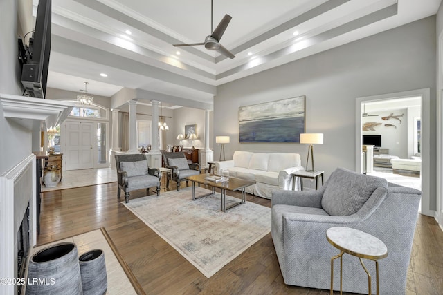 living room with a towering ceiling, ceiling fan with notable chandelier, decorative columns, a raised ceiling, and dark wood-type flooring