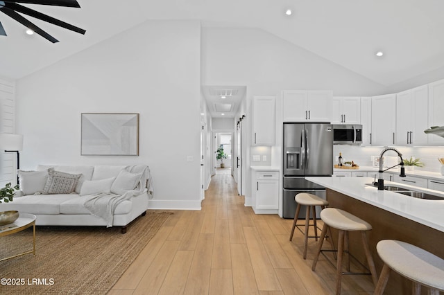 kitchen with a kitchen bar, a sink, high vaulted ceiling, white cabinets, and stainless steel appliances