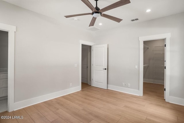 unfurnished bedroom featuring ceiling fan, a spacious closet, a closet, and light hardwood / wood-style flooring