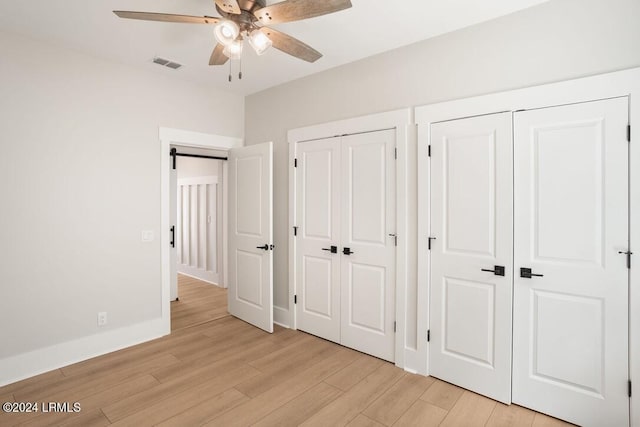 unfurnished bedroom with multiple closets, a barn door, ceiling fan, and light hardwood / wood-style floors