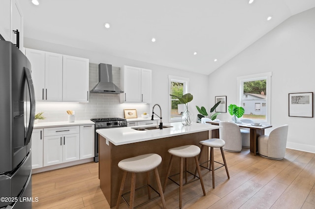 kitchen with wall chimney range hood, a healthy amount of sunlight, a sink, stainless steel gas range, and freestanding refrigerator