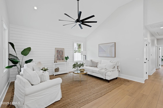 living area featuring high vaulted ceiling, light wood-style flooring, attic access, a ceiling fan, and baseboards