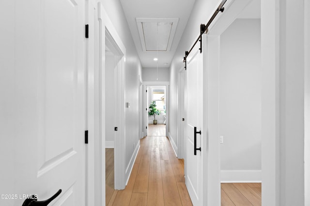 hallway with light wood-style floors, attic access, baseboards, and a barn door