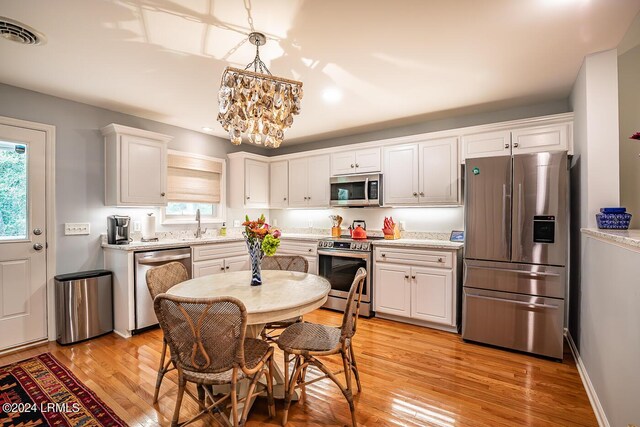 kitchen featuring pendant lighting, appliances with stainless steel finishes, white cabinetry, light stone counters, and light hardwood / wood-style floors