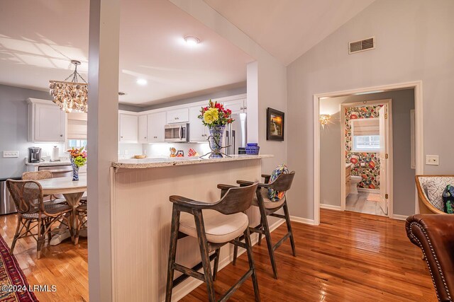 kitchen with white cabinetry, a kitchen bar, hardwood / wood-style floors, and light stone counters