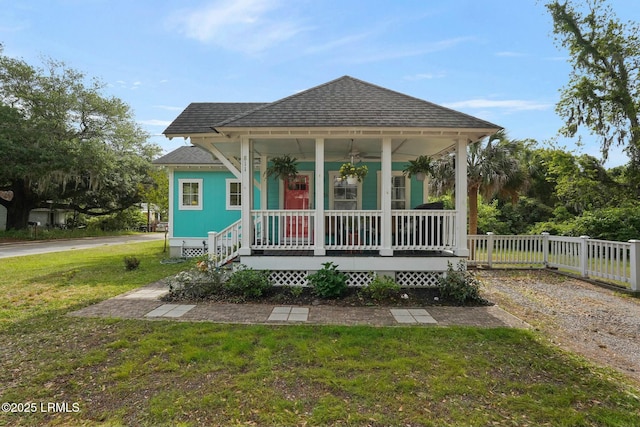 bungalow with a front yard, a shingled roof, covered porch, and fence