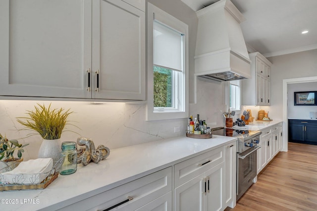 kitchen featuring light hardwood / wood-style flooring, premium range hood, high end range, backsplash, and white cabinets