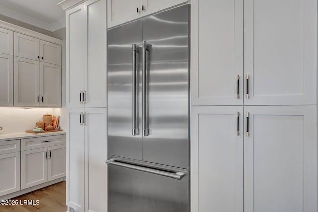 kitchen featuring built in fridge, white cabinetry, decorative backsplash, crown molding, and light wood-type flooring