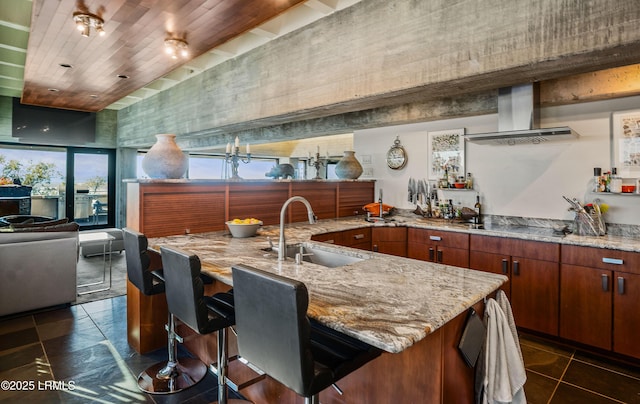 kitchen featuring extractor fan, a breakfast bar, an island with sink, sink, and dark tile patterned floors