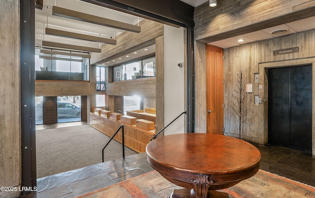 dining space featuring beam ceiling, elevator, a fireplace, and wood walls