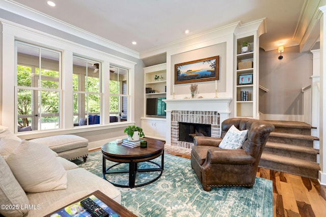 living room featuring light wood-type flooring, a brick fireplace, crown molding, and built in features