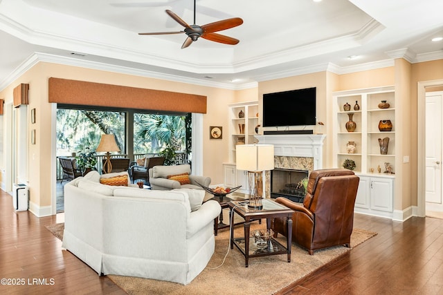 living room featuring crown molding, hardwood / wood-style floors, a tray ceiling, and a fireplace