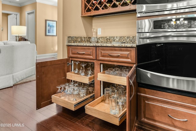 kitchen featuring light stone counters, dark hardwood / wood-style flooring, ornamental molding, and stainless steel oven