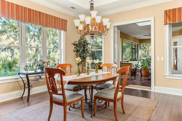 dining area featuring baseboards, visible vents, wood-type flooring, crown molding, and ceiling fan with notable chandelier