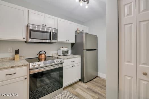 50 Pebble Beach Cv Unit F111, Bluffton, SC 29910 - kitchen with appliances with stainless steel finishes, white cabinetry, light wood-style floors, and light stone counters