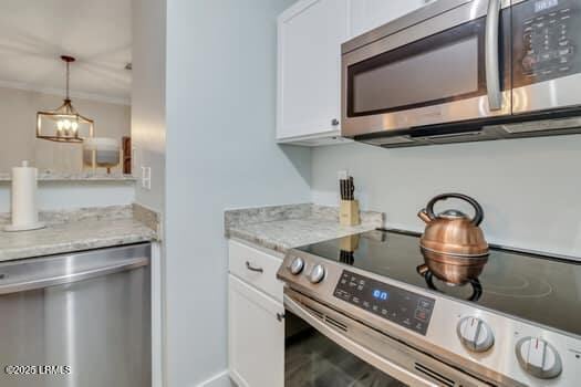 50 Pebble Beach Cv Unit F111, Bluffton, SC 29910 - kitchen with appliances with stainless steel finishes, white cabinetry, light stone countertops, decorative light fixtures, and crown molding