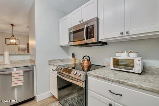 50 Pebble Beach Cv Unit F111, Bluffton, SC 29910 - kitchen featuring appliances with stainless steel finishes, white cabinetry, light stone counters, light wood-type flooring, and hanging light fixtures