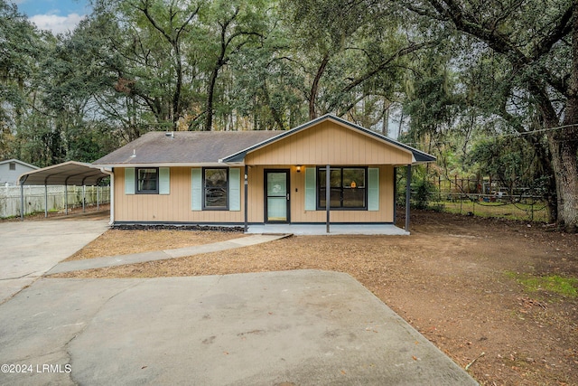 view of front of house with roof with shingles, concrete driveway, covered porch, fence, and a carport