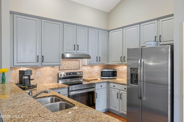 kitchen featuring appliances with stainless steel finishes, a sink, under cabinet range hood, and light stone countertops