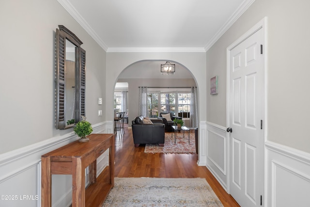 entryway with arched walkways, a wainscoted wall, ornamental molding, wood finished floors, and a chandelier