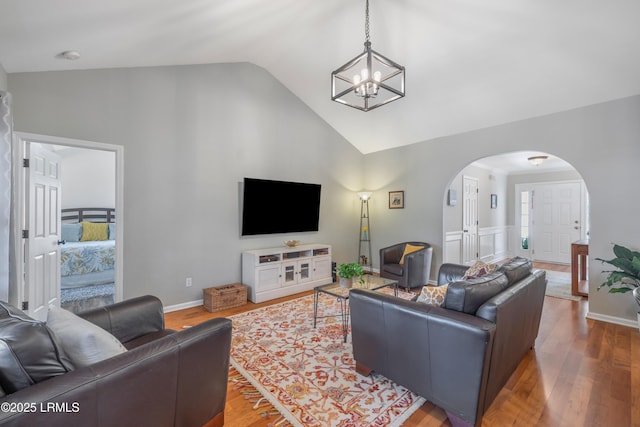 living room with arched walkways, vaulted ceiling, wood finished floors, and an inviting chandelier