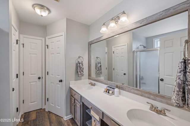 bathroom with a stall shower, wood finished floors, a sink, and double vanity