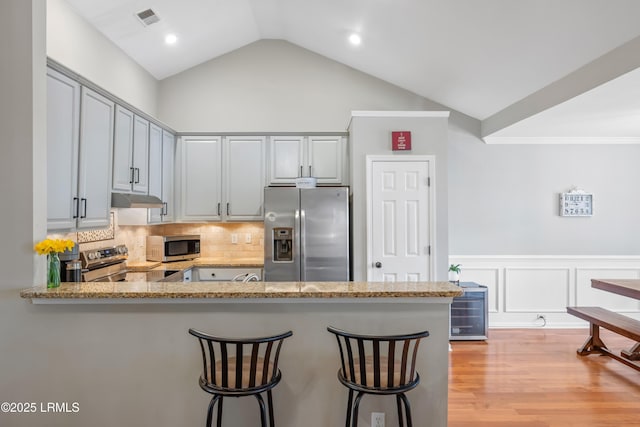 kitchen featuring stainless steel appliances, visible vents, a peninsula, under cabinet range hood, and a kitchen bar