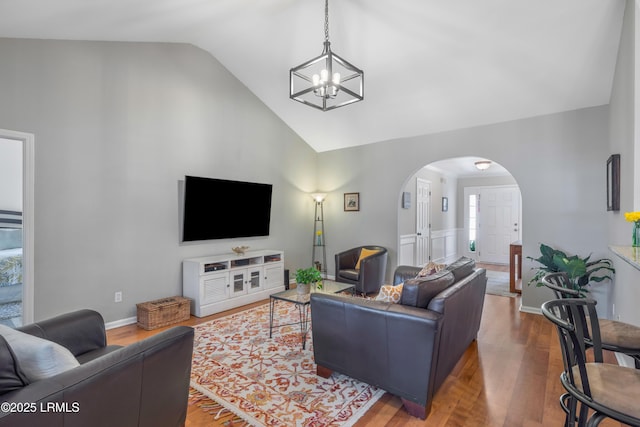 living area featuring arched walkways, wood finished floors, lofted ceiling, and an inviting chandelier