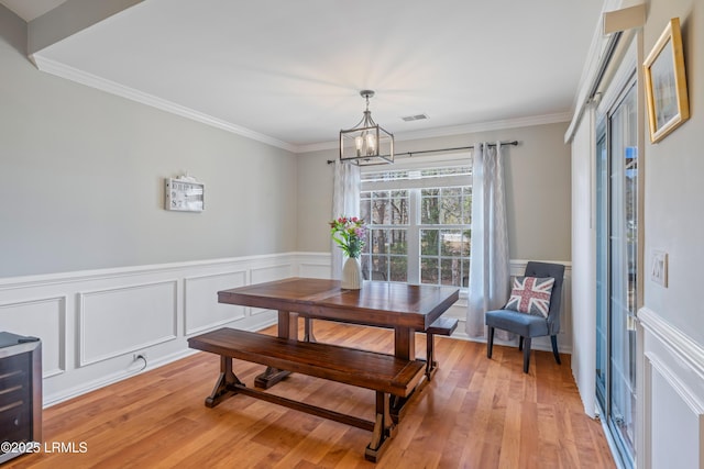 dining room with ornamental molding, light wood finished floors, visible vents, and a notable chandelier