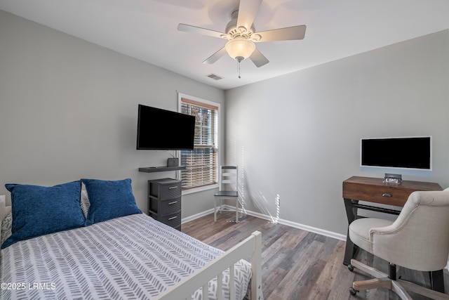 bedroom with a ceiling fan, visible vents, baseboards, and wood finished floors