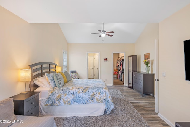 bedroom featuring baseboards, lofted ceiling, wood finished floors, a walk in closet, and a closet