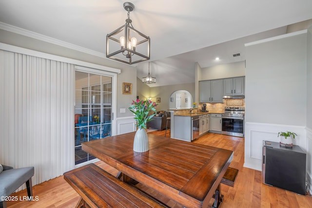 dining area featuring arched walkways, crown molding, a notable chandelier, light wood-style flooring, and wainscoting