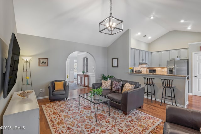 living room with arched walkways, high vaulted ceiling, wood finished floors, and baseboards