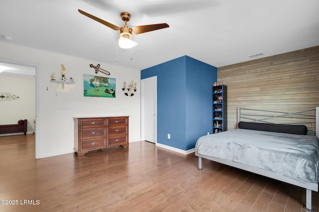 bedroom with wood walls, wood finished floors, visible vents, and baseboards
