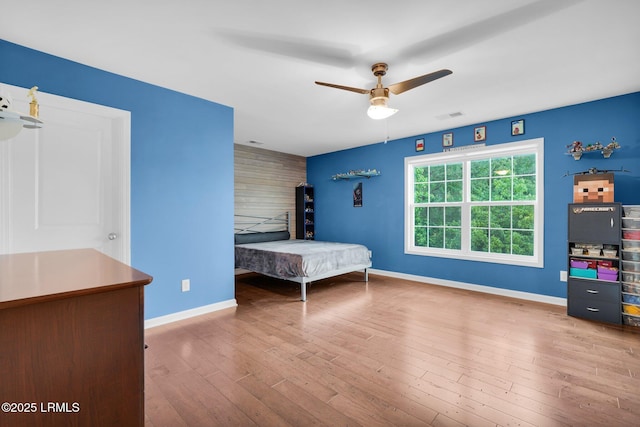 bedroom with a ceiling fan, visible vents, baseboards, an accent wall, and wood finished floors