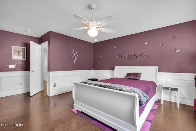 bedroom with hardwood / wood-style floors, wainscoting, and a decorative wall