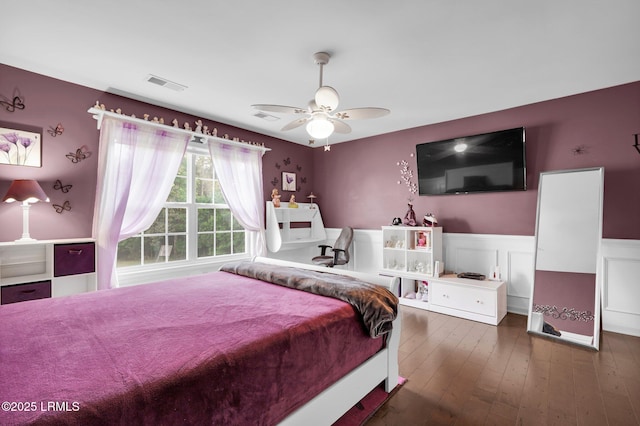 bedroom with hardwood / wood-style floors, visible vents, a wainscoted wall, and a ceiling fan