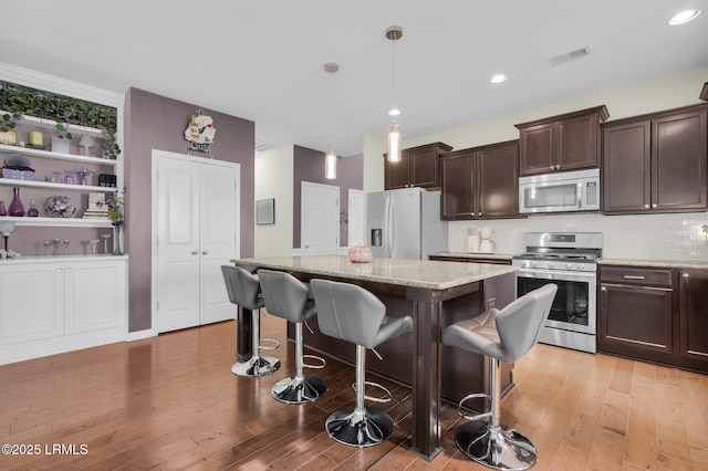 kitchen with a breakfast bar area, appliances with stainless steel finishes, dark brown cabinets, a center island, and visible vents