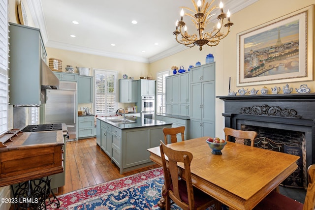 kitchen with sink, stainless steel appliances, light hardwood / wood-style floors, a center island with sink, and decorative light fixtures