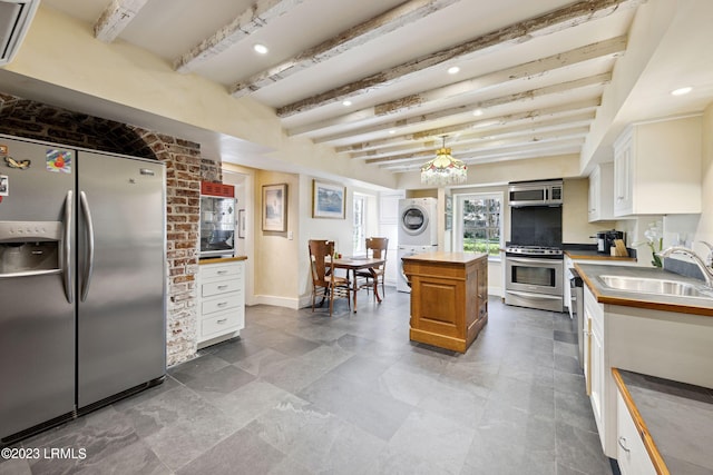 kitchen featuring stacked washing maching and dryer, beamed ceiling, white cabinetry, a center island, and stainless steel appliances